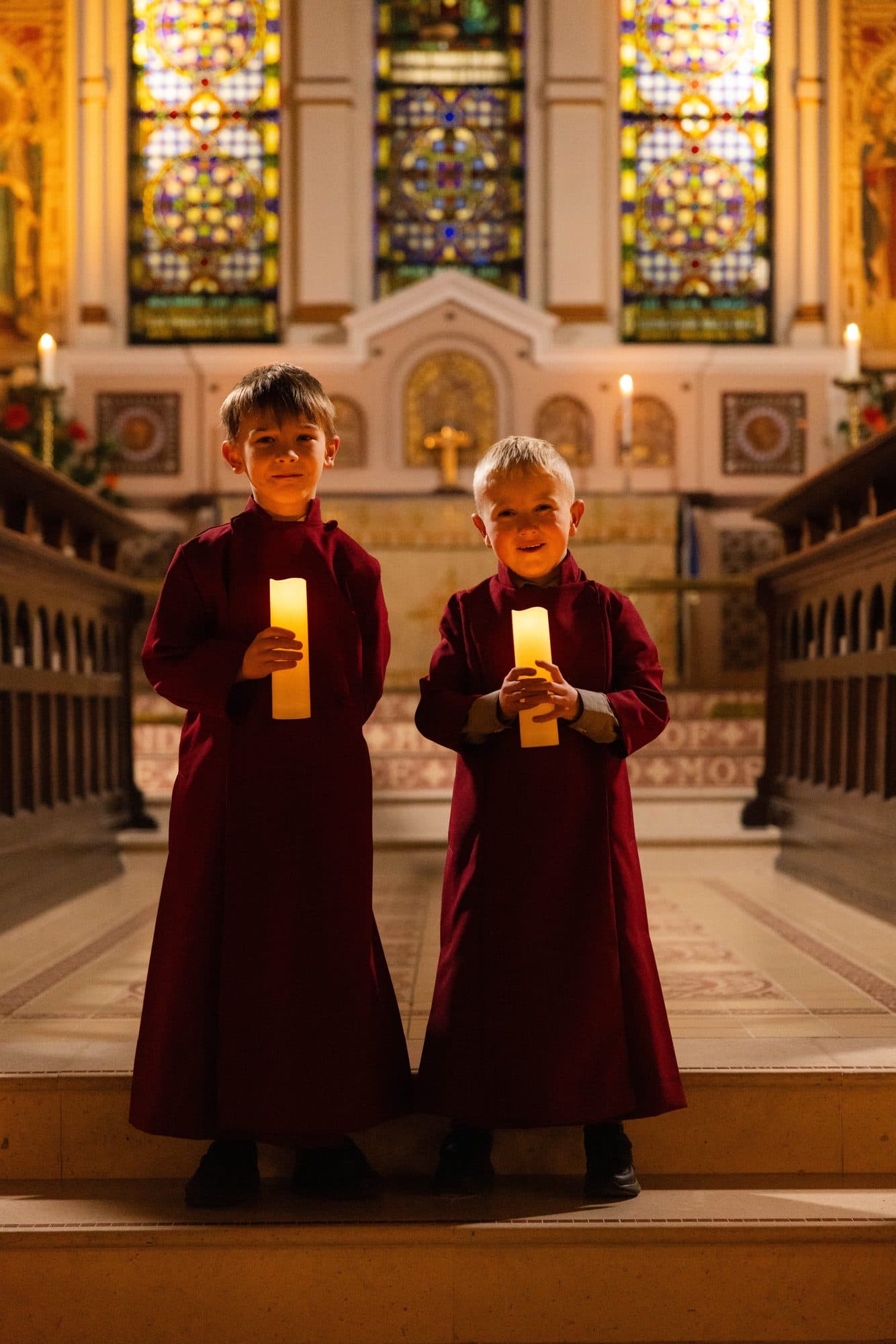 Two young choristers in red cassocks holding candles